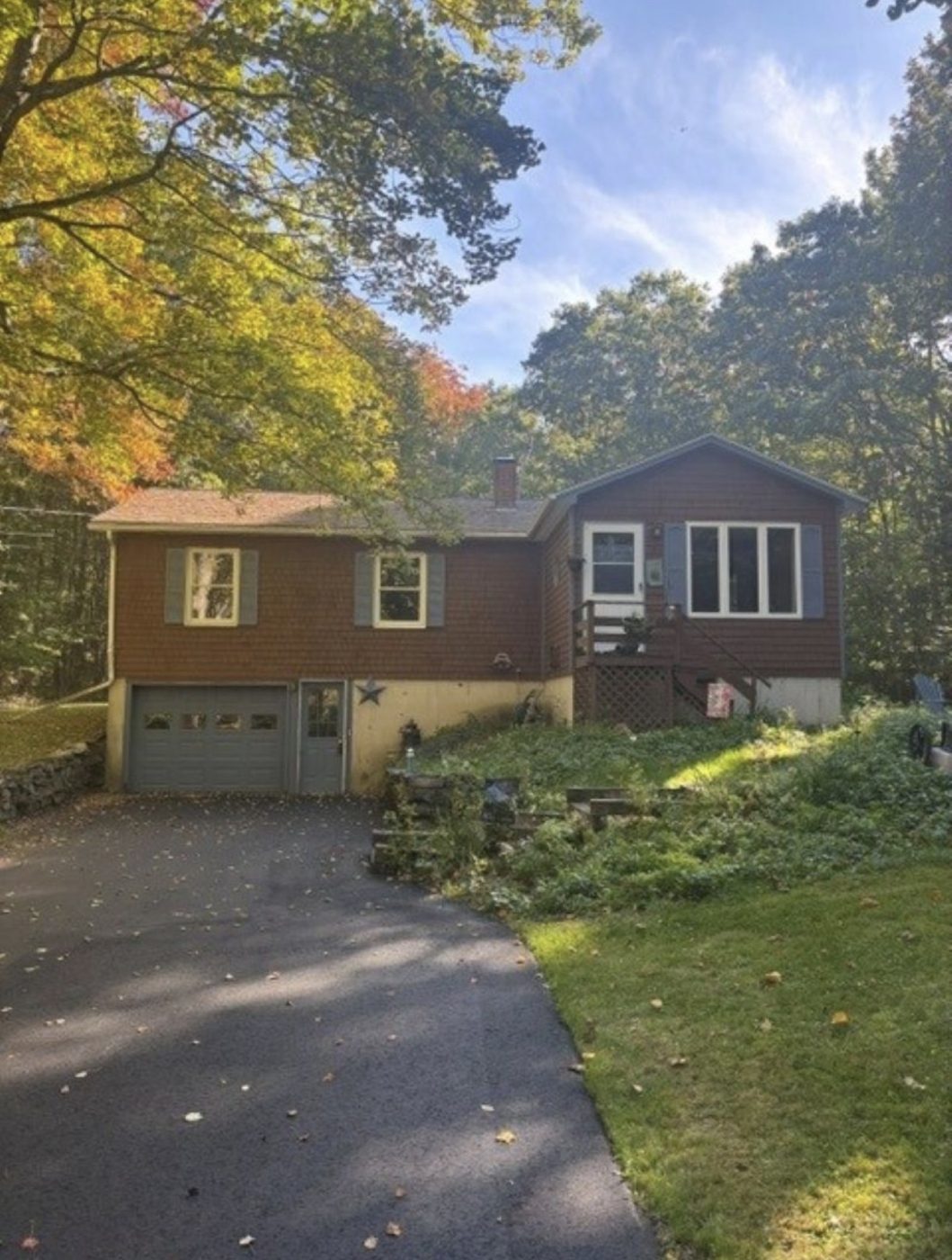 Front of the house with attached garage and paved driveway, fall trees behind